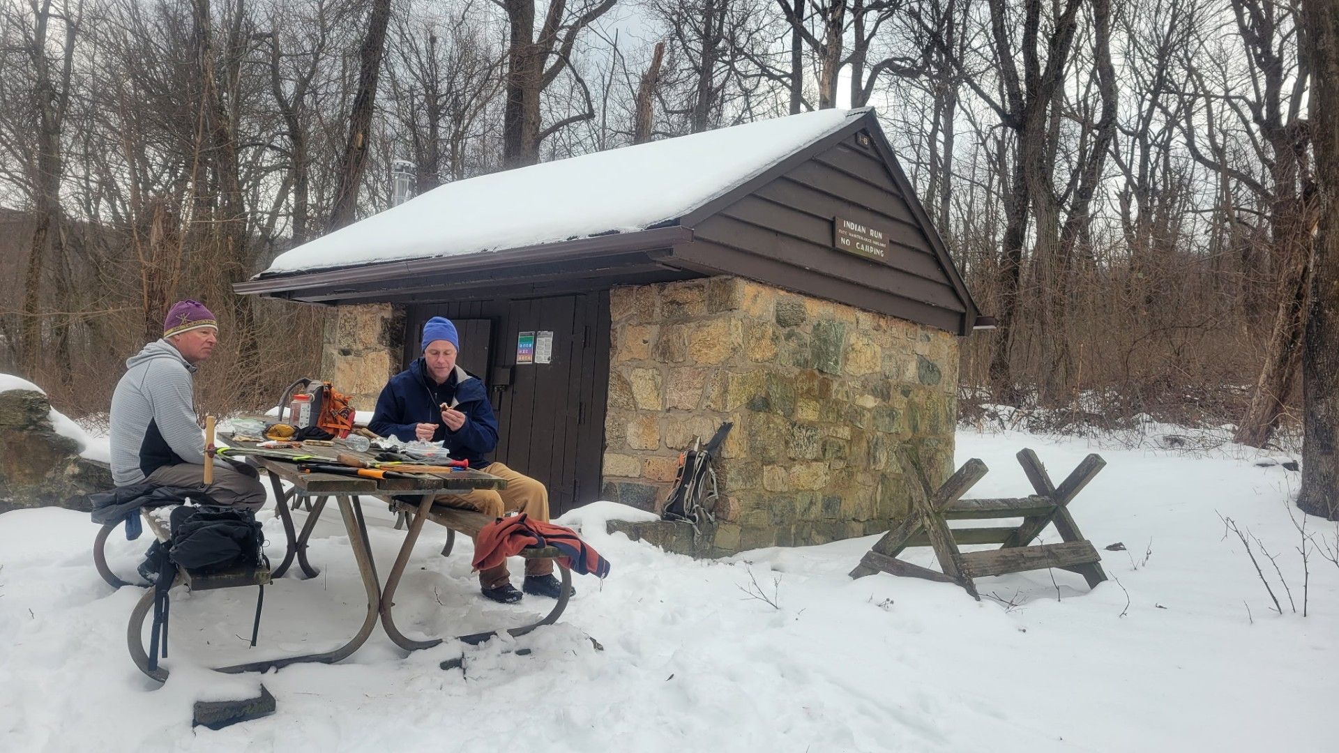Two people are sitting at a picnic table in the snow.