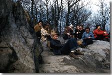 A group of people are sitting on a rock in the woods.