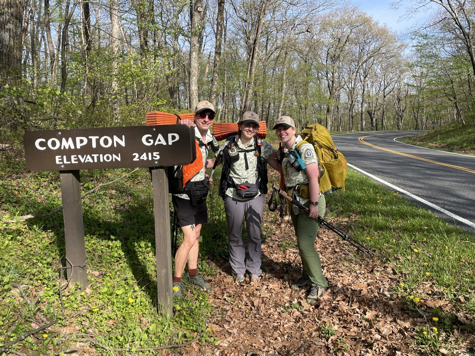 Three people are standing in front of a sign that says compton gap elevation 2415.