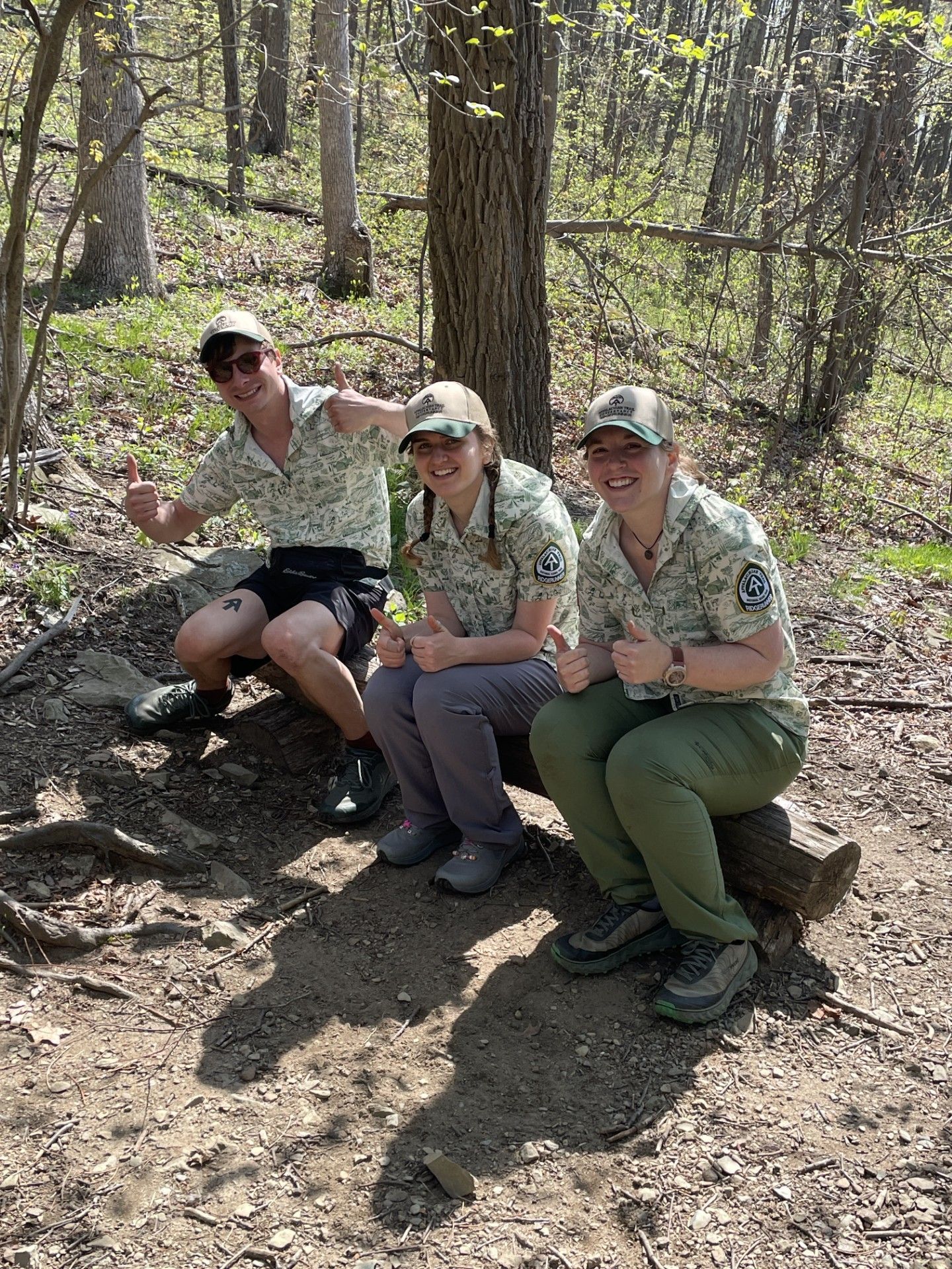 Three people are sitting on a bench in the woods.