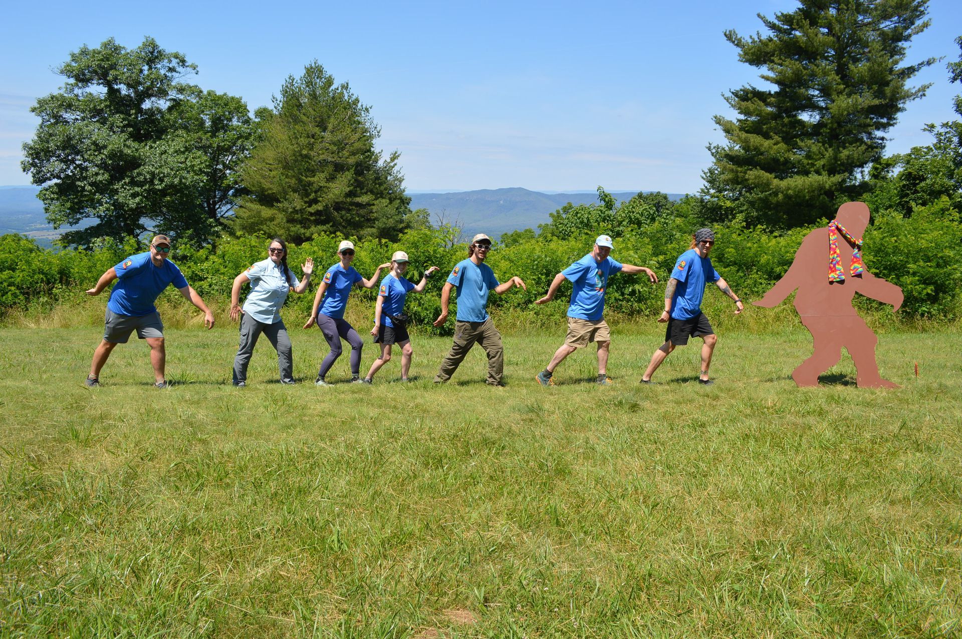 A group of people in blue shirts are standing in a grassy field.