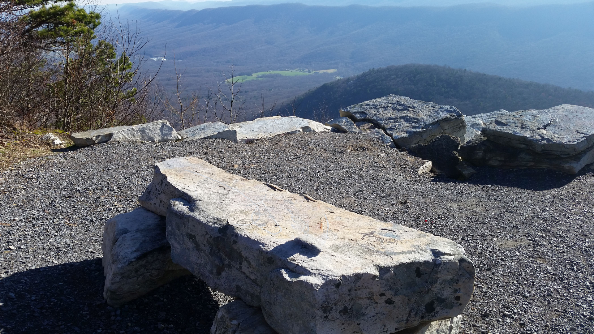A stone bench is sitting on top of a rocky hill overlooking a mountain range.