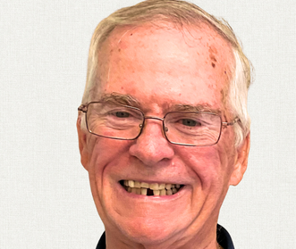 A smiling person wearing glasses, centered against a light, neutral background.
