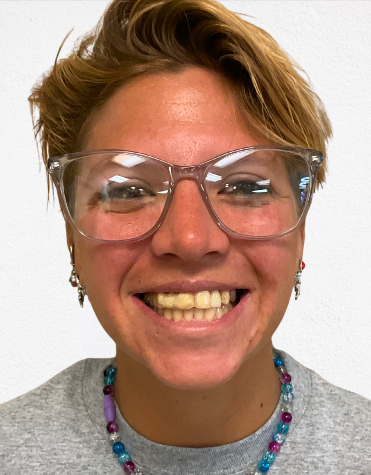 A person with short light hair wearing clear-framed glasses and a colorful beaded necklace, smiling at the camera.