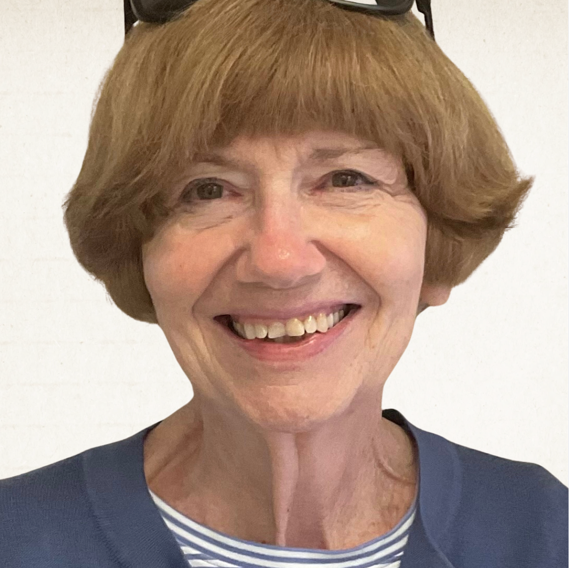 A person with chin-length reddish-brown hair and glasses perched on their head, smiling warmly against a white background.