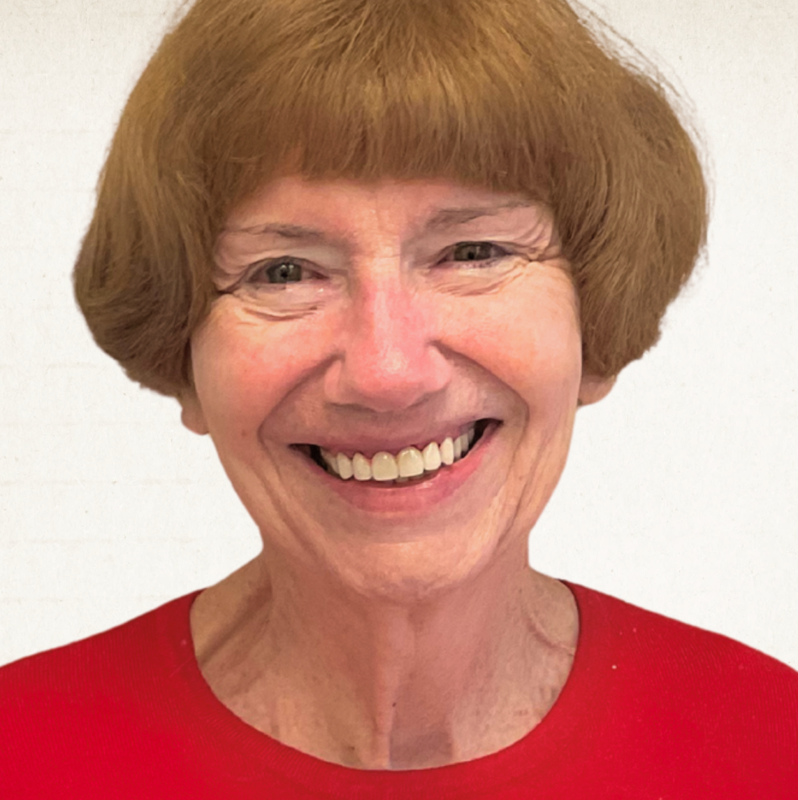A smiling person with shoulder-length reddish-brown hair, wearing a red shirt against a plain white background.