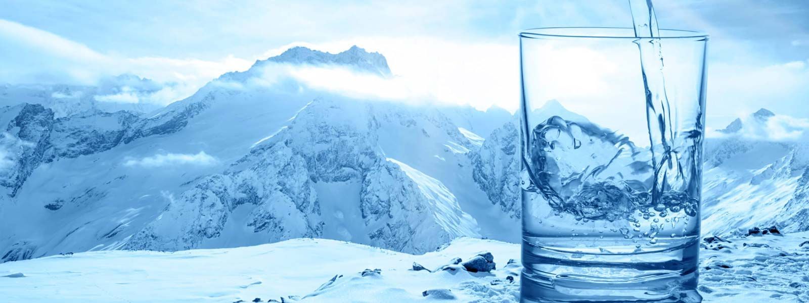 Paesaggio montano innevato con un bicchiere d'acqua limpida in primo piano.