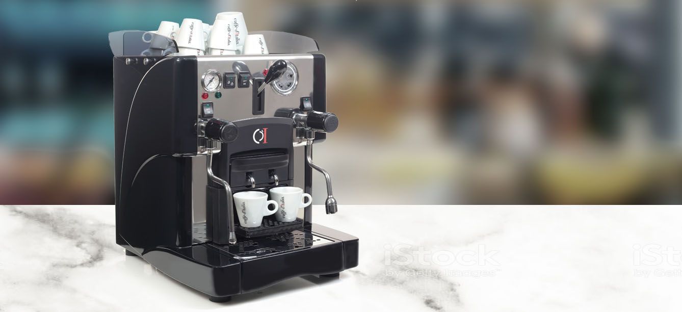 Macchina per caffè espresso compatta di colore nero su un bancone, con uno sfondo sfocato di un bar.