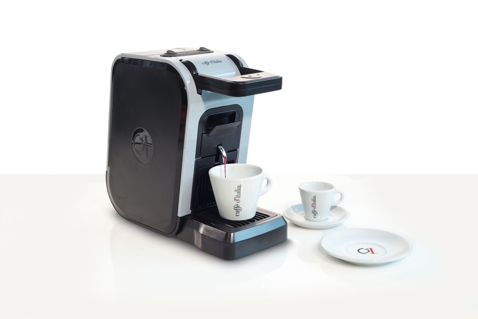 Macchina da caffè nera che eroga il caffè in una tazza, con due tazze e piattini bianchi su una superficie bianca.