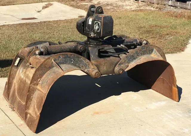 A large claw bucket is sitting on a sidewalk.