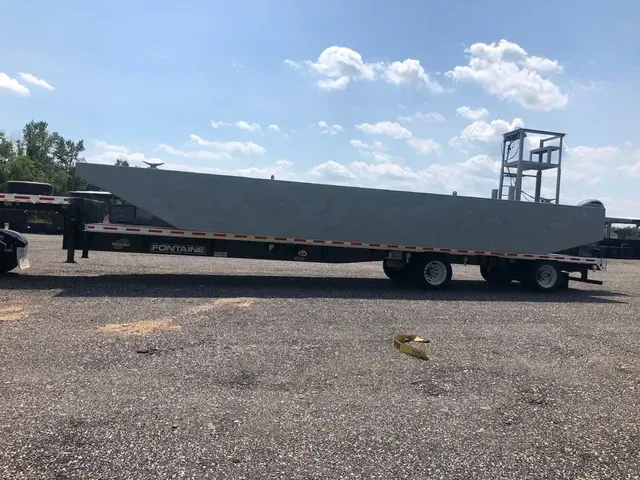 A large gray trailer is parked in a gravel lot.