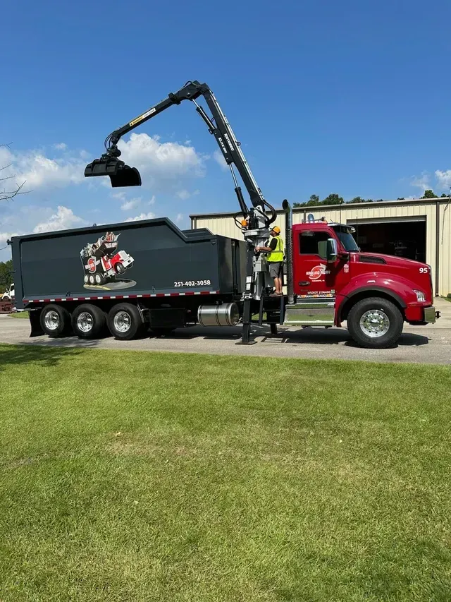 A red dump truck with a crane attached to it is parked on the side of the road.