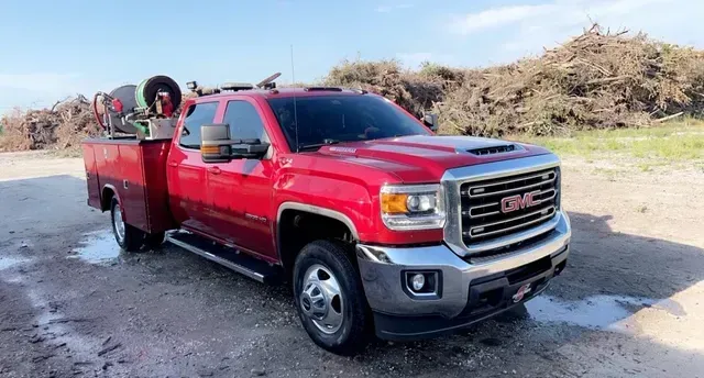 A red gmc truck is parked in front of a pile of wood.