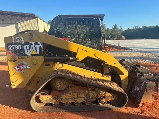 A yellow cat track loader is parked on a dirt road.
