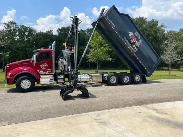 A dump truck with a crane attached to it is parked on the side of the road.