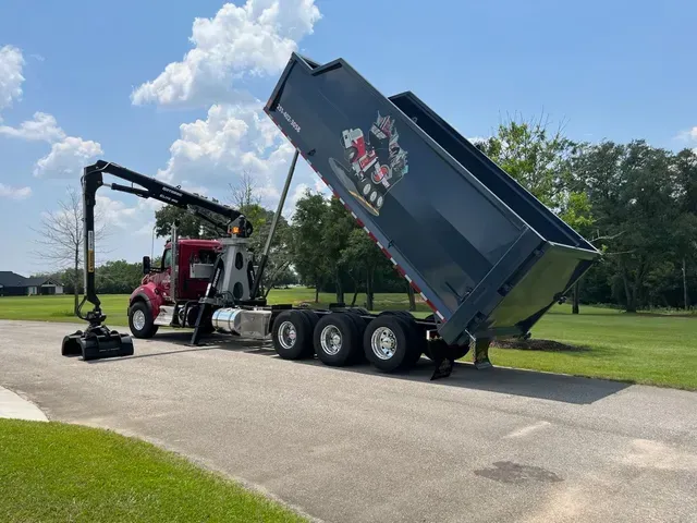 A dump truck with a crane attached to it is parked in a driveway.