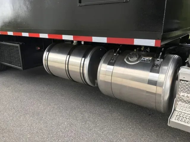 A black truck with stainless steel fuel tanks is parked on the side of the road.