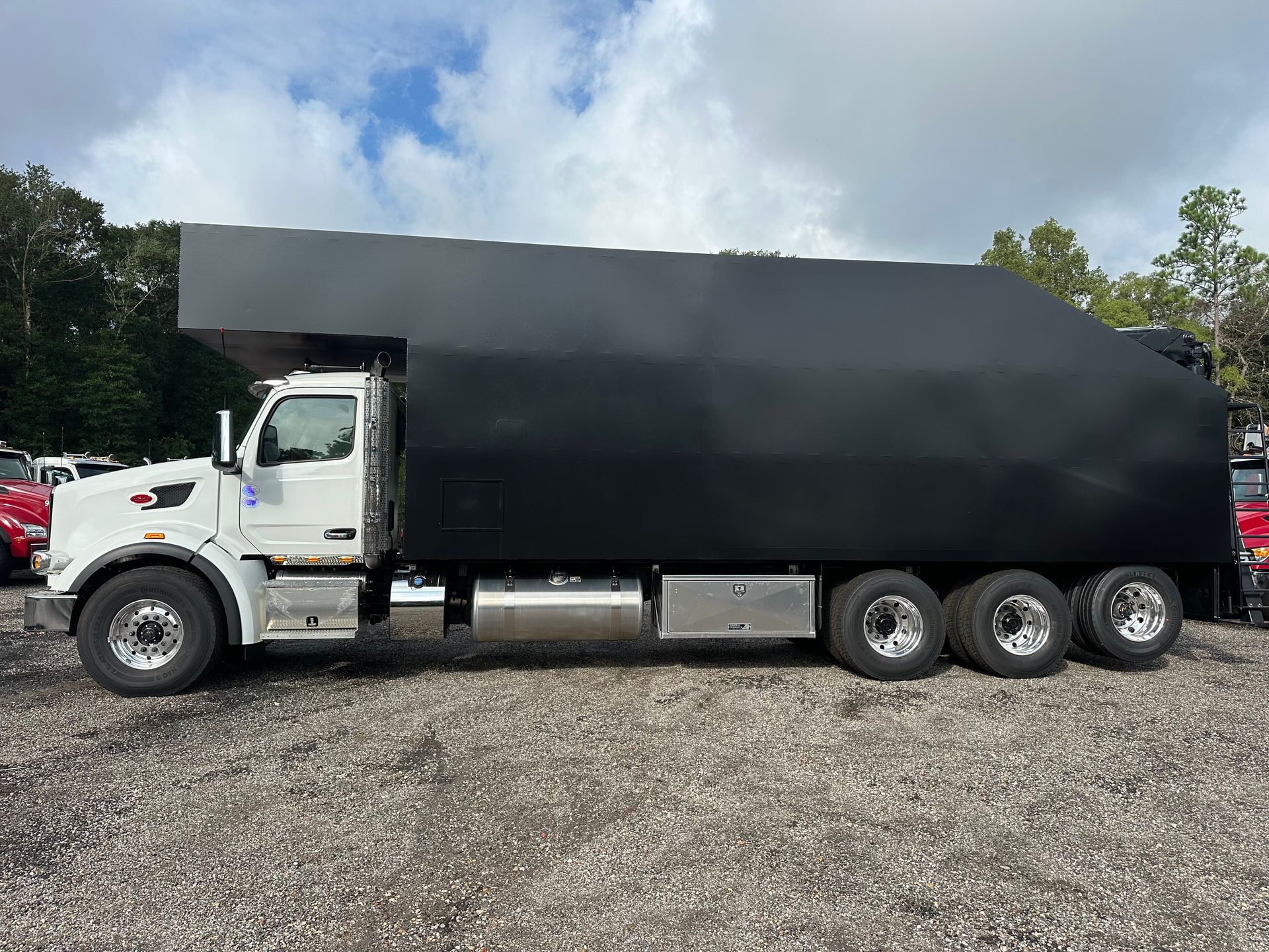 A white truck with a black tarp on top of it is parked in a gravel lot.