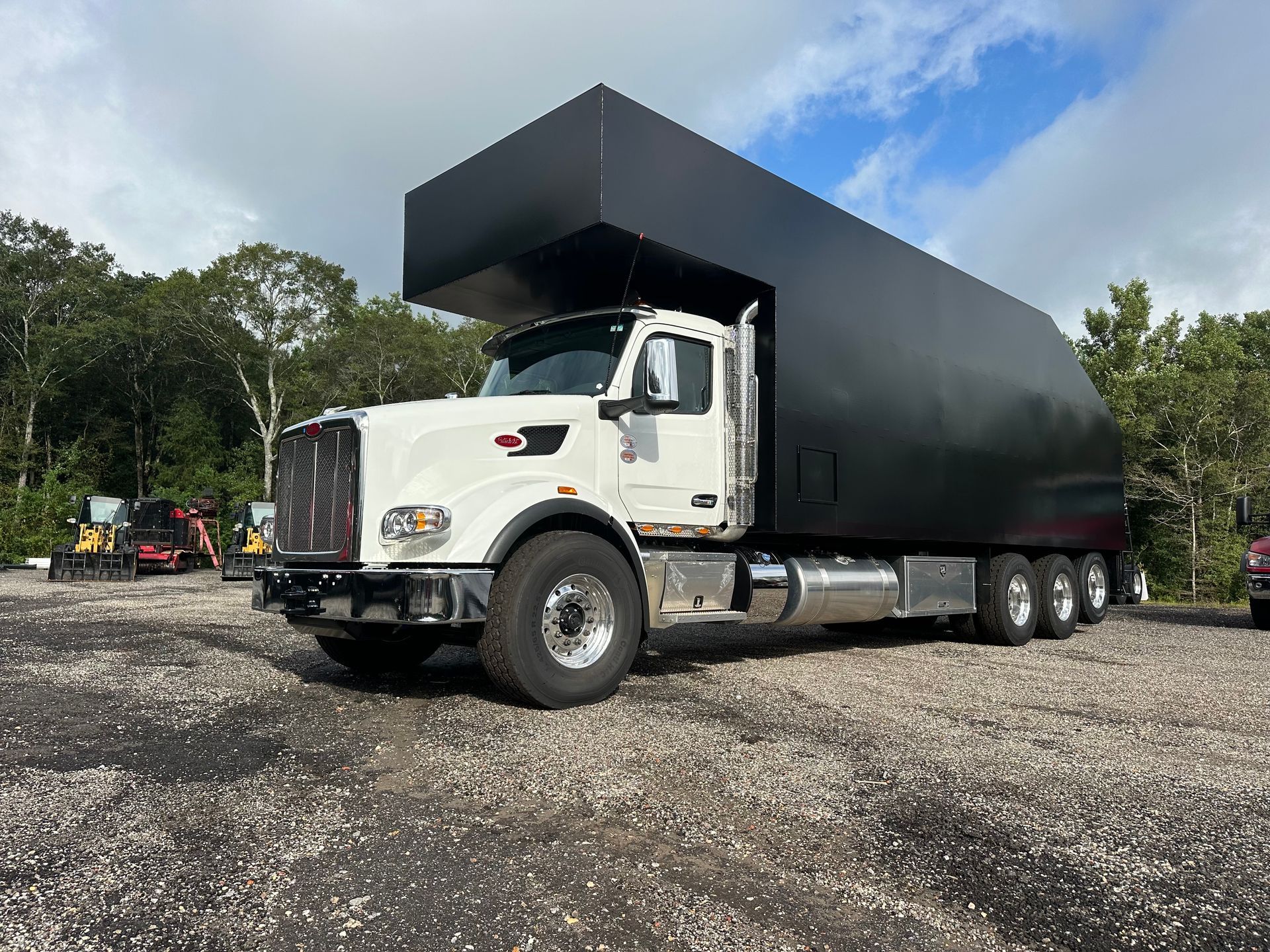A white truck with a black tarp on top of it is parked in a gravel lot.