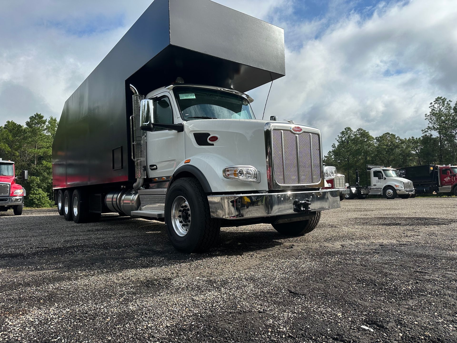A white semi truck with a black trailer is parked in a gravel lot.