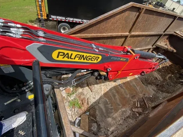 A red palfinger crane is sitting on top of a dumpster.