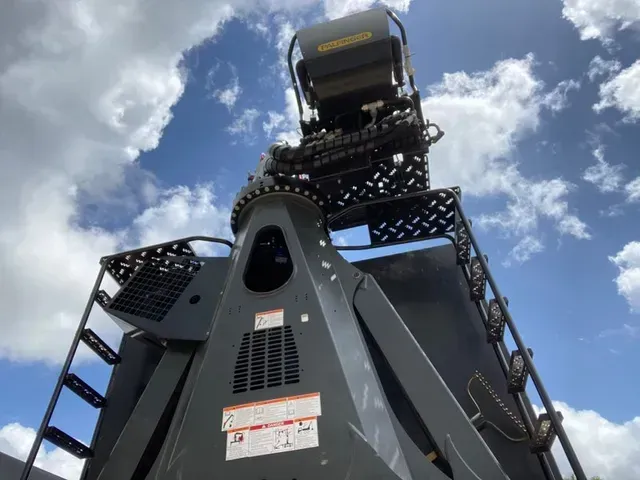 A large black machine is sitting in front of a blue sky with clouds.