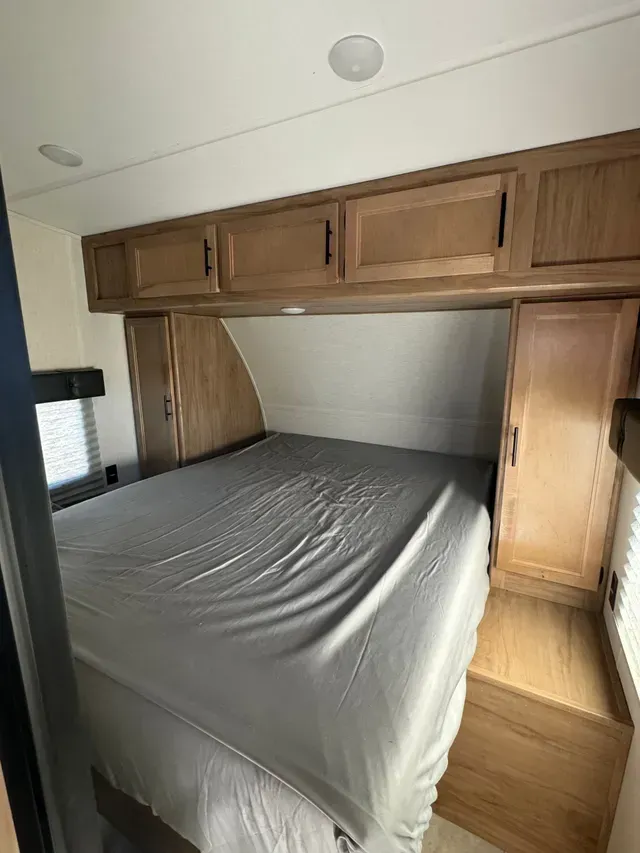 A bedroom in a trailer with a bed and cabinets.