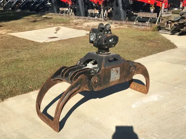 A large metal claw is sitting on a sidewalk next to a grassy field.
