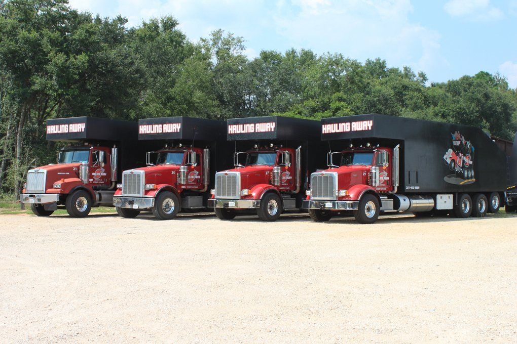 Debris Removal Services - A row of red semi trucks parked next to each other on a dirt road.