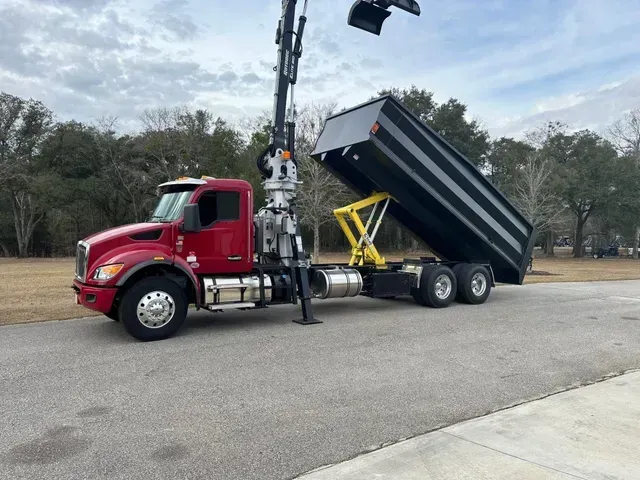 A red dump truck with a crane attached to it is parked on the side of the road.