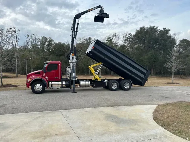 A dump truck with a crane attached to it is parked on the side of the road.