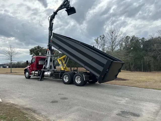 A dump truck with a crane attached to it is parked on the side of the road.