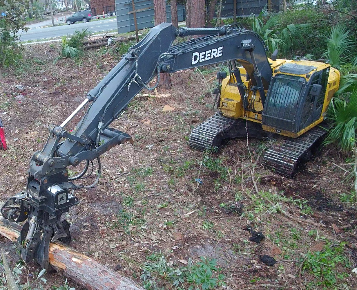 A deere excavator is sitting in the middle of a forest.
