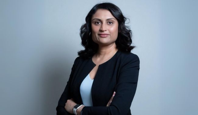 A woman in a black jacket is standing with her arms crossed