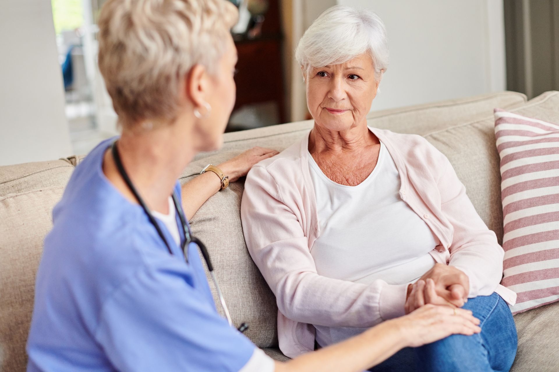 An elderly woman is sitting on a couch talking to a nurse.