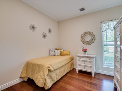 A bedroom with a single bed , dresser , nightstand and window.