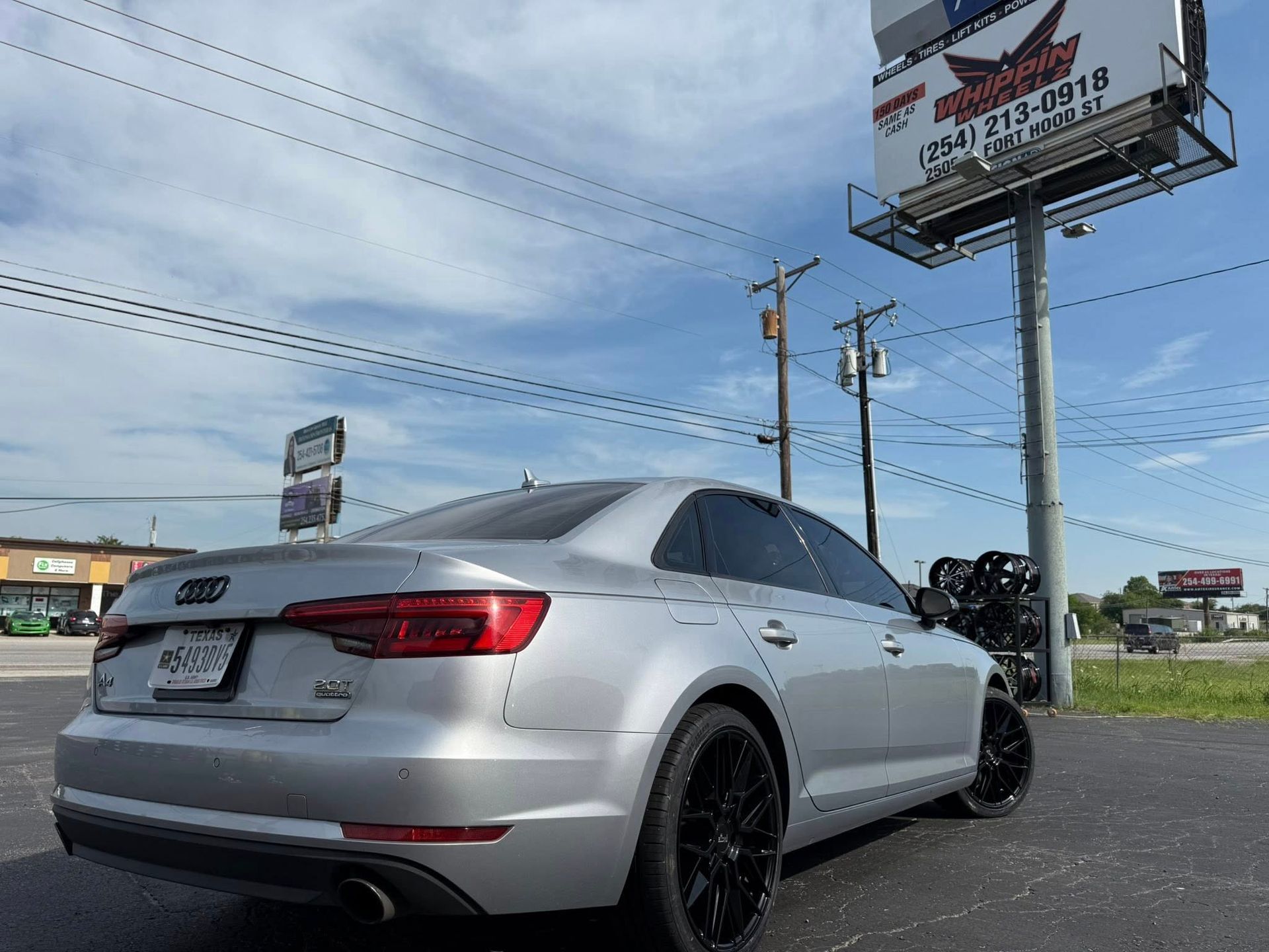 A silver audi a4 is parked in front of a billboard.