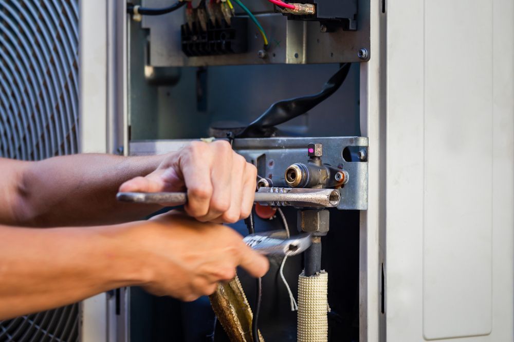 Hands using tools to repair an electrical panel with exposed wiring and cables.