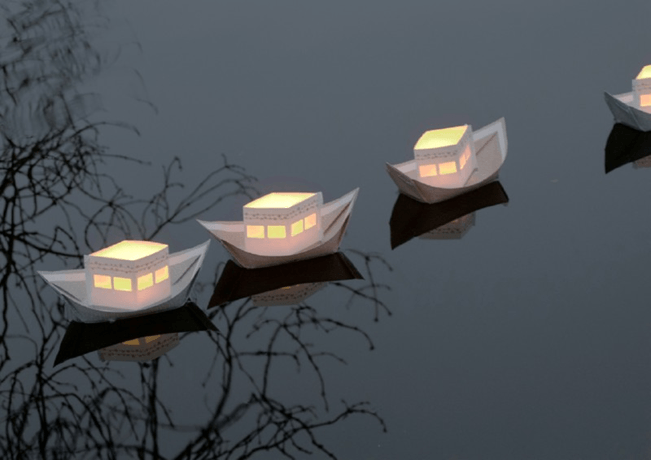 Maanlicht kinderuitvaart - afbeelding op de homepagina van 3 witte  varende wensbootjes van papier met lichtje