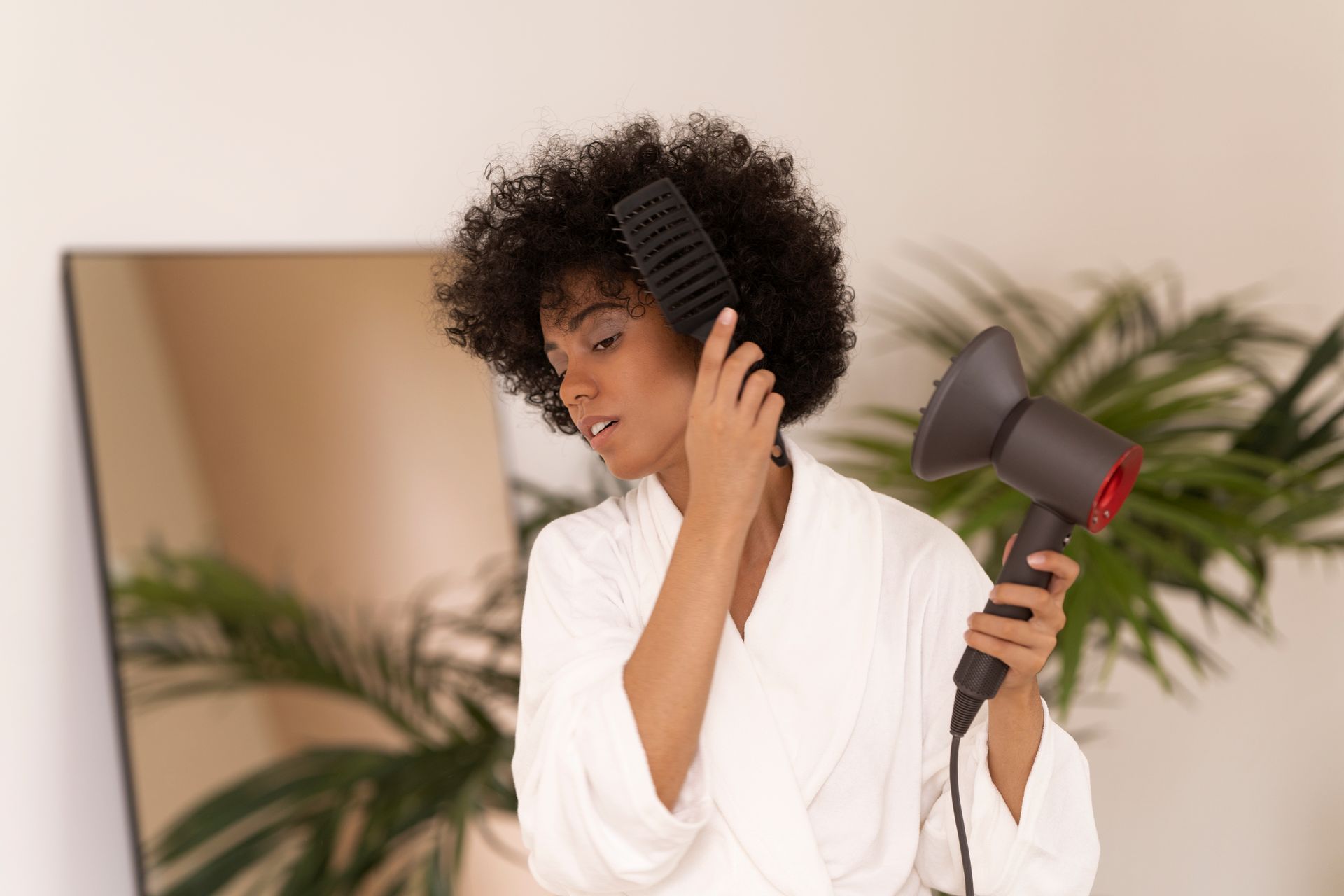 Mulher usando secador com bocal difusor e escova para finalizar o cabelo e reduzir o frizz em casa.