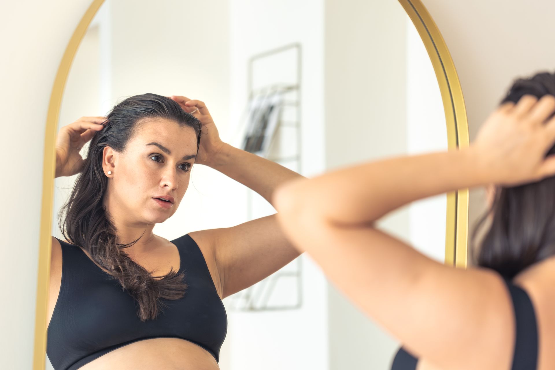 Mulher olhando o cabelo no espelho após o treino representando os cuidados capilares na academia