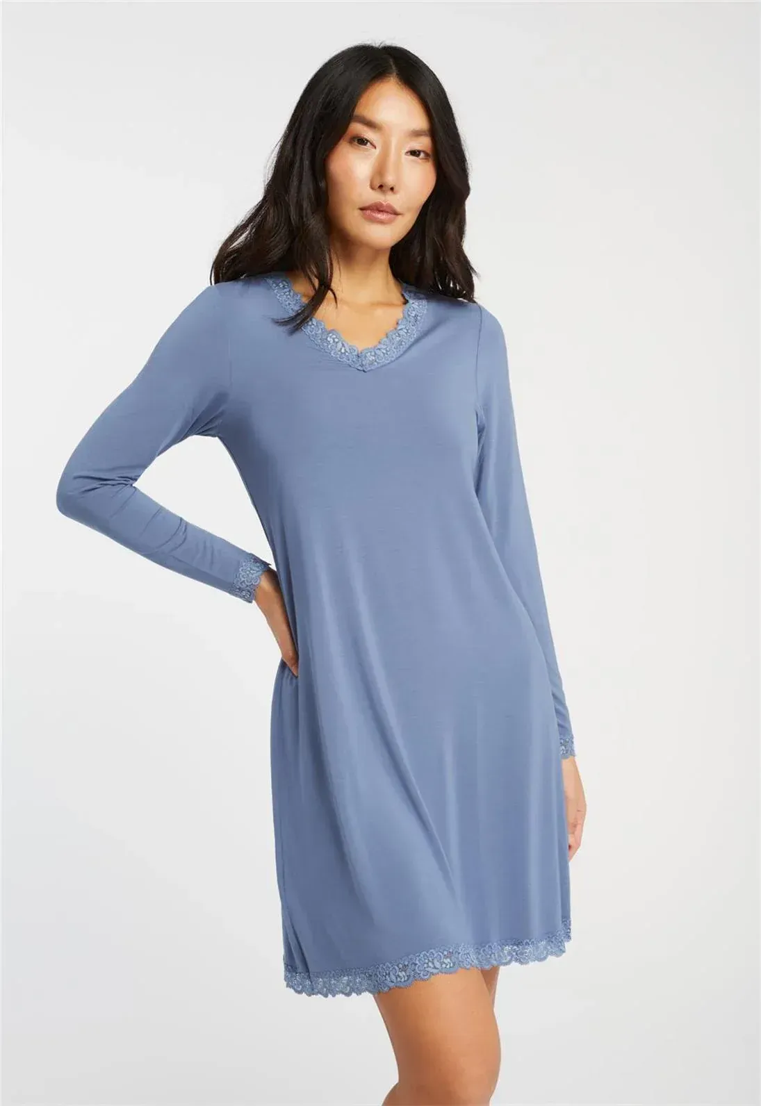 Woman in blue long-sleeved nightgown, hands on hip. The gown has lace trim. Light background.