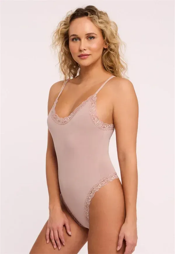 Woman wearing a pink bodysuit with lace trim, standing against a white backdrop.