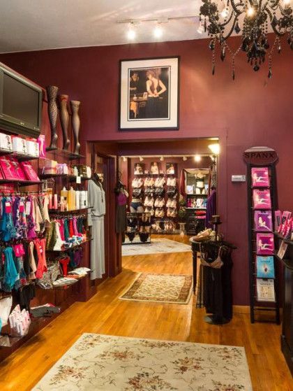 Lingerie shop interior: shelves of undergarments, doorway to more displays, burgundy walls, chandelier.