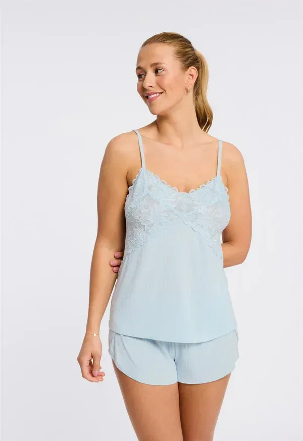 Woman in light blue camisole and shorts, smiling, posing in front of a white background.