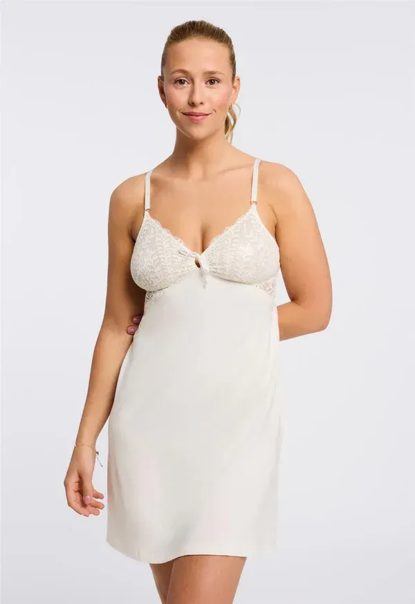 Woman wearing a cream-colored slip dress with lace details, standing in a studio setting.