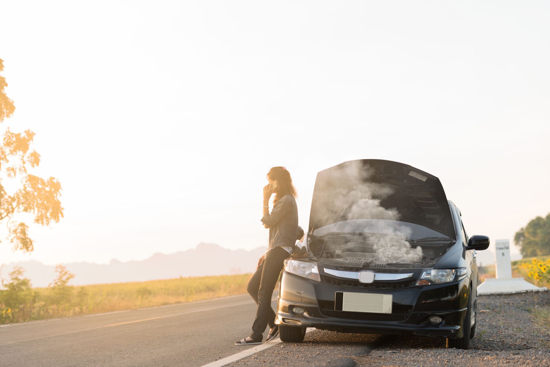 Person stands beside a black car with its hood open on a roadside at sunset. | Chuck's Garage