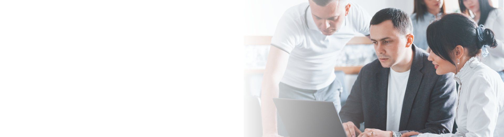 A group of people are sitting around a table looking at a laptop.