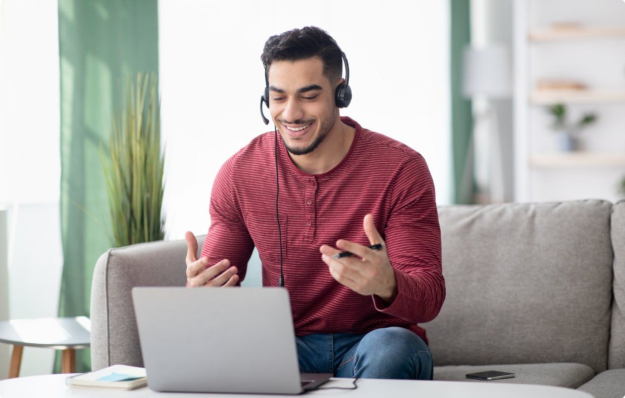A man wearing headphones is sitting on a couch using a laptop computer.