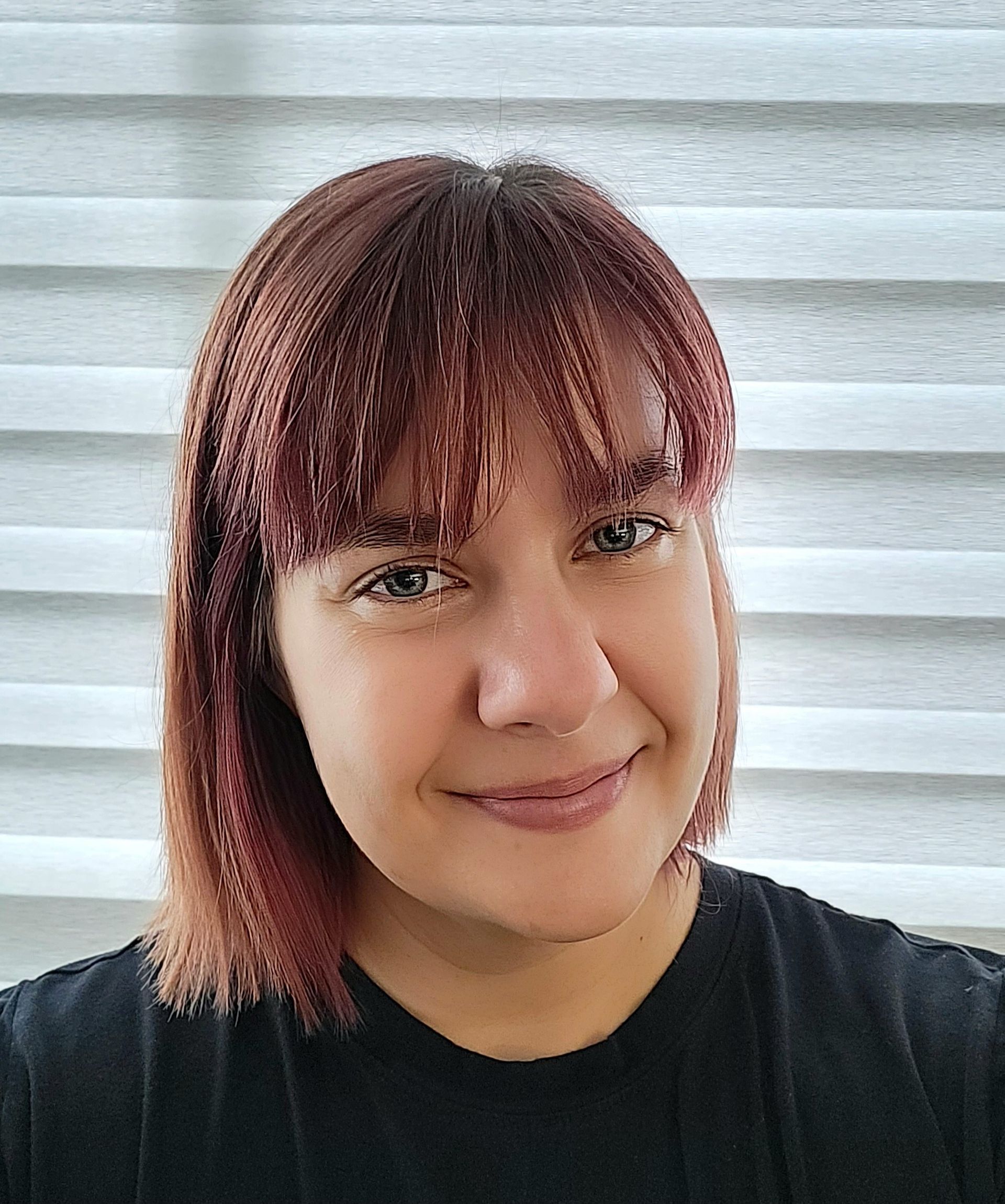 A woman with red hair is smiling and wearing a black shirt.